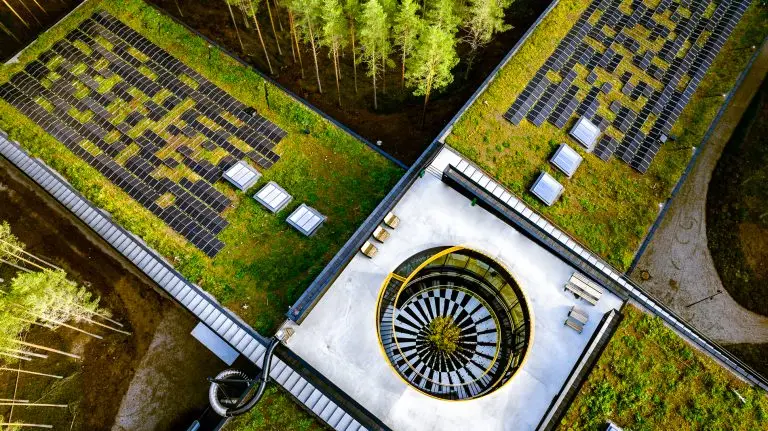 Dronebilde der man ser et utsnitt av bygget "The Plus" på Magnor. Bygget har sedum på taket, takvinduer og solpanel. Bygget er formet som et pluss-tegn og ligger tett på naturen.